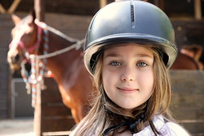 Girl in horse riding helmet with horse in background
