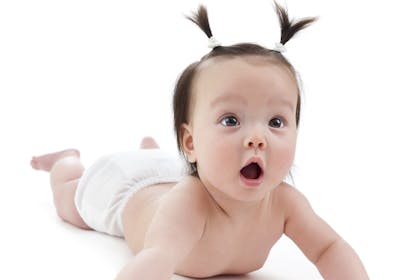 Cute baby with pigtails and a surprised expression enjoying tummy-time