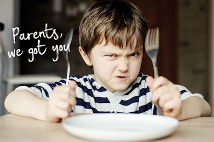 Boy holding knife and fork up next to empty plate