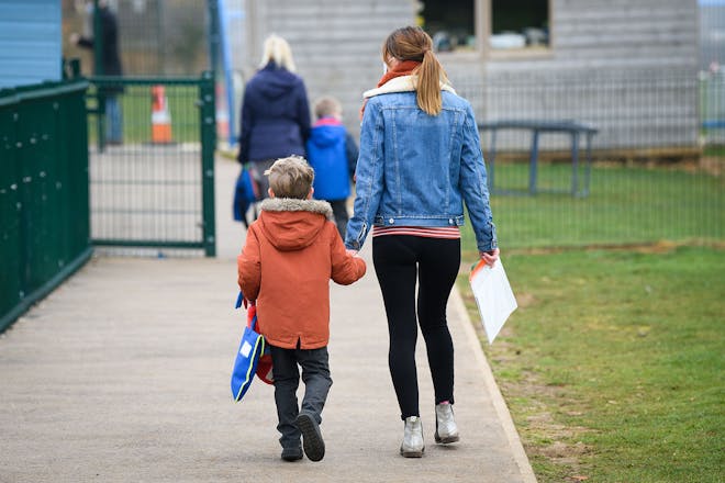 Mum and young son holding hands and walking into school
