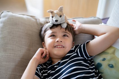 Boy lies on sofa with toy dog