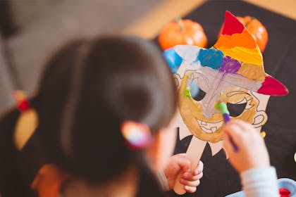 A toddler paints a witch mask for a Halloween craft activity