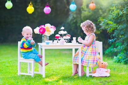 A toddler and a young child enjoying a tea party in the garden