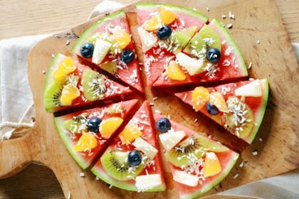 Circle of watermelon cut into slices and decorated with fruit and coconut so it looks like a pizza