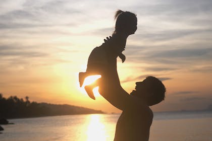 Silhouette of dad throwing daughter up in air by lake