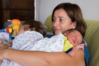 Mother at home holding her newborn son and 3 year old daughter