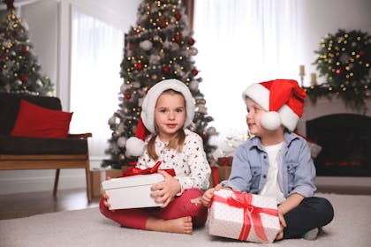 Two children holding presents in front of a Christmas tree