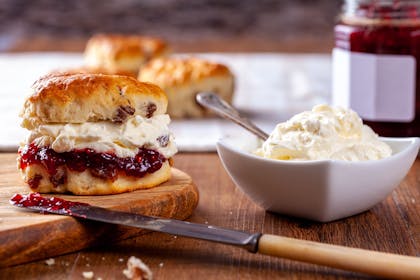 Scone with clotted cream and jam next to bowl of clotted cream