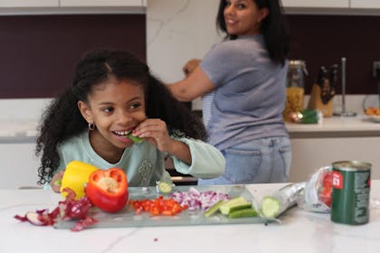Child in kitchen with mum eating healthy raw vegetables and salad
