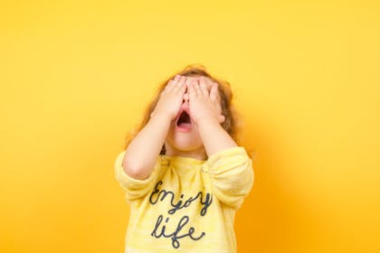 Toddler with their hands on their face and a yellow background