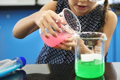 Young girl pouring coloured liquid between beakers in science experiment