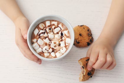 Kids hands holding cup of hot chocolate and cookie