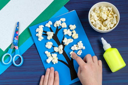 child sticking popcorn to card with tree drawn on
