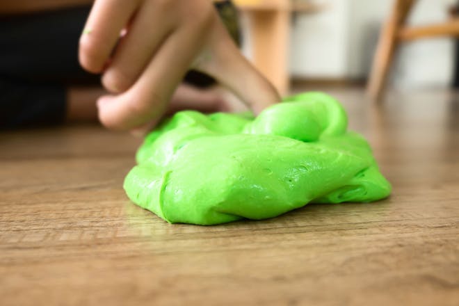 Child playing with green slime on wooden floor