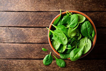 Fresh spinach leaves in a bowl on a wooden table. 