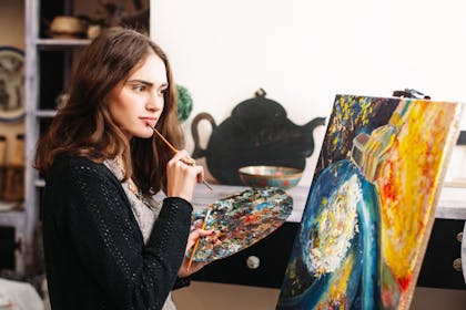 Painter holding paint palette next to painted canvas on easel