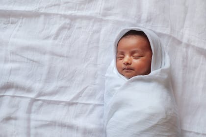 Newborn baby swaddled in white blanket 