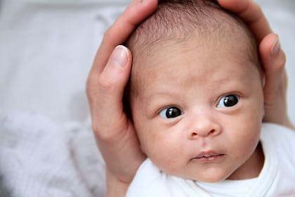 Newborn mixed race baby, head cradled in mother's hands