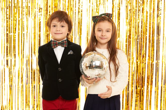 Boy and girl stand in front of gold foil curtain dressed in formal clothes and holding a disco ball