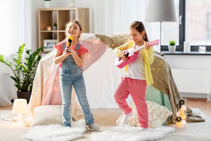 Two young girls with microphone and guitar performing in front room