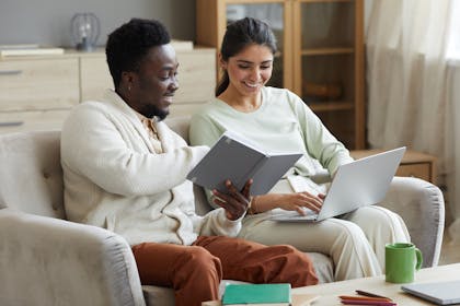 A smiling couple sitting on the sofa with a laptop and book