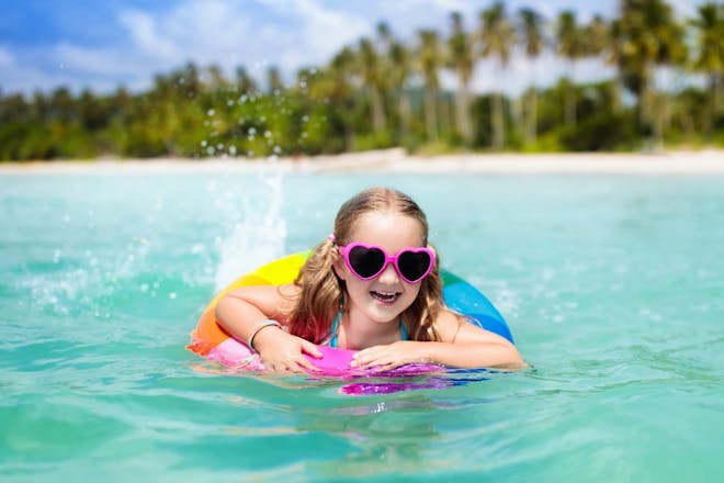 A smiling young girl in shades swims in a blue sea with a rubber ring