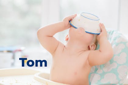 Baby in high chair tipping bowl of food into mouth. Name Tom written in text