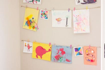 Wall display with children's artwork hanging by pegs