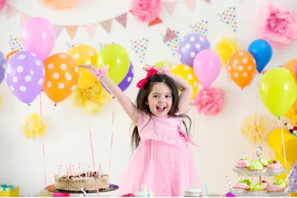 happy girl in pink dress with arms up with balloons behind her