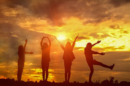 Teenagers spelling out the word Love with their arms against sunset