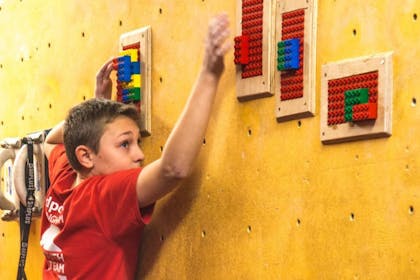 A young boy in a red t-shirt grips a lego-themed climbing wall at Redpoint Climbing Centre