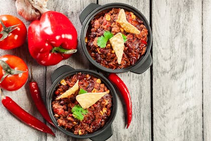 Two bowls of chilli con carne surrounded by chillis
