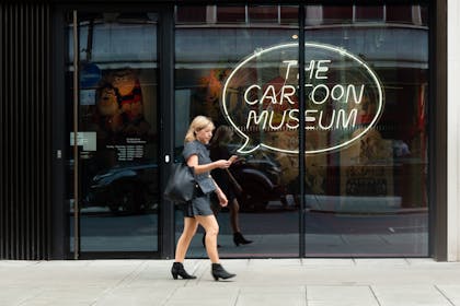 A woman is looking at her phone as she walks past The Cartoon Museum in London