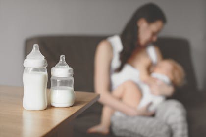 Mum breastfeeding baby with bottles of formula in the foreground