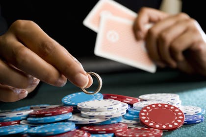 Hand holding wedding ring with gambling chips and cards
