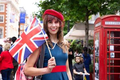 A smiling woman wearing red, white and blue, holds a union flag at a street party in London 