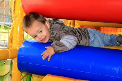 Toddler climbing through tight gap in soft play