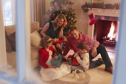 family sitting in living room with christmas tree behind them and fire in the fire place