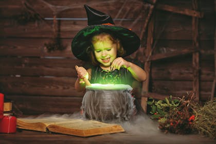 Child dressed up as a witch dropping a spider int her cauldron