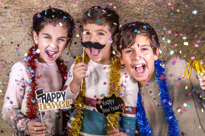Kids at new year's eve party with confetti, tinsel, fake moustaches and signs saying 'Happy new year'