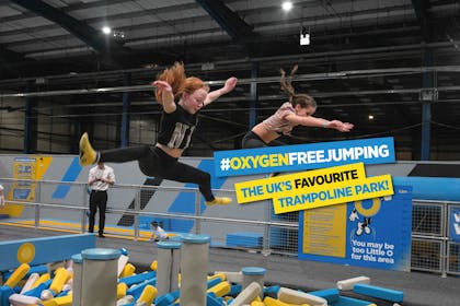 Two girls bouncing over foam pit on trampolines