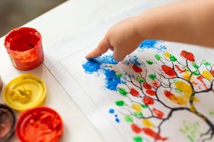 child painting leaves on tree using finger tips