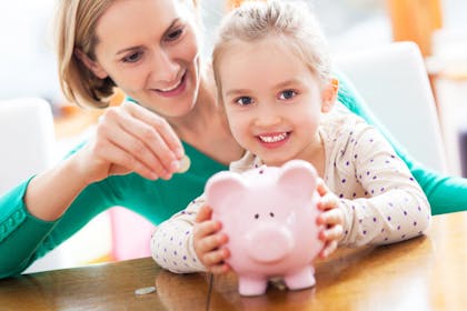 Woman helping daughter put money in piggy bank