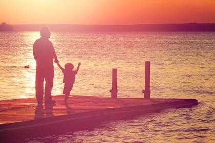 Man and child standing on jetty at sunset