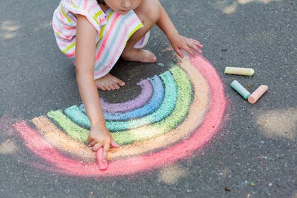 Girl draaing rainbow on pavement using chalk