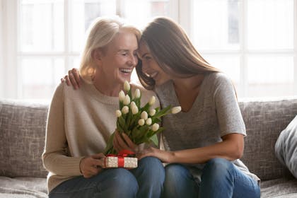 Mum and daughter sitting together and laughing, with flowers and a gift for Mother's Day