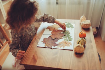 Little girl sticking autumn leaves onto paper 