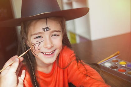 Girl in witch costume with spider face paint for Halloween