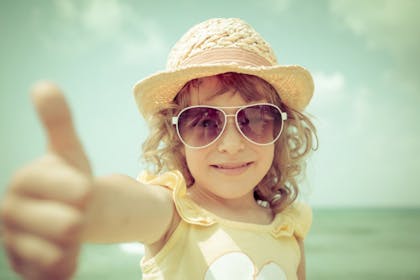 girl at the beach with sunhat and shades giving thumbs up