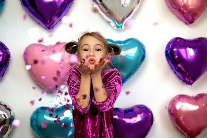 Heart-shaped balloons and a child blowing confetti